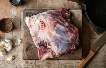 A whole, raw, wild venison shoulder on a chopping board.