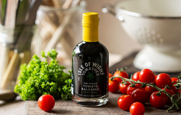 A bottle of Isle of Wight, Oak Smoked Tomato Balsamic Vinegar with tomatoes and parsley.