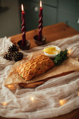 Baked trout wellington on a wooden board with candles and decorative elements on a soft fabric background
