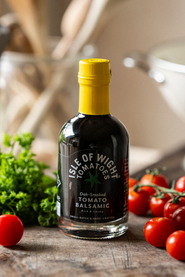 A bottle of Isle of Wight, Oak Smoked Tomato Balsamic Vinegar with tomatoes and parsley.
