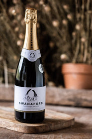 A bottle of Swanaford Classic Cuvée sparkling wine standing on a chopping board.
