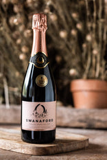 A bottle of Swanaford Brut Rosé sparkling wine standing on a chopping board.
